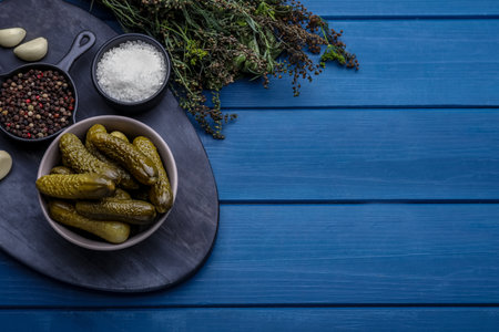 Bowl of pickled cucumbers and ingredients on blue wooden table, flat lay. Space for textの写真素材