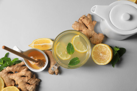 Delicious ginger tea and ingredients on light gray background, flat lay