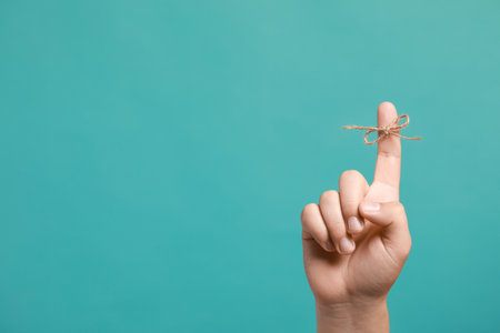 Man showing index finger with tied bow as reminder on turquoise background, closeup. Space for textの写真素材
