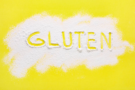 Word Gluten written with flour on yellow background, top viewの写真素材