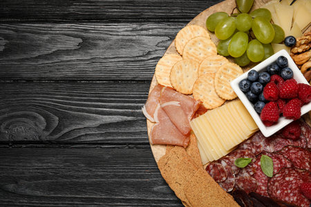Snack set with delicious Parmesan cheese on black wooden table, top view. Space for text