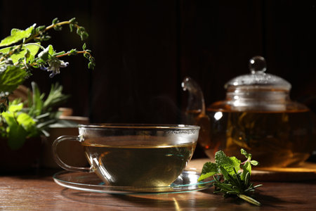 Cup of aromatic herbal tea, mint and rosemary on wooden tableの写真素材