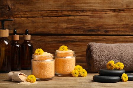 Jars with orange sea salt, spa stones, towel and beautiful flowers on wooden tableの写真素材