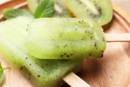 Tasty kiwi ice pops on wooden plate, closeup. fruit ice lollyの写真素材