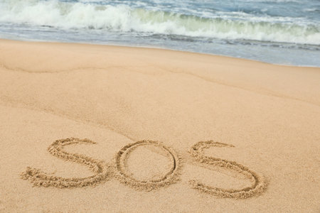 Message SOS drawn on sand near the sea