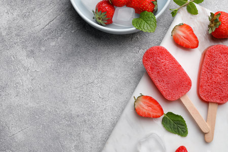 Tasty fruit ice pops with strawberries on gray table, flat lay. Space for textの写真素材