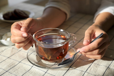 Woman holding spoon near glass cup with tea bag at table, closeupの写真素材