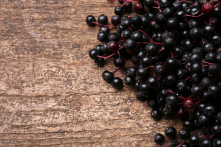 Pile of tasty elderberries (Sambucus) on wooden table, closeup. Space for textの写真素材