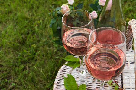 Glasses and bottle of delicious rose wine on picnic basket outdoors, closeup. Space for textの写真素材