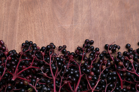 Tasty elderberries (Sambucus) on wooden table, top view. Space for text