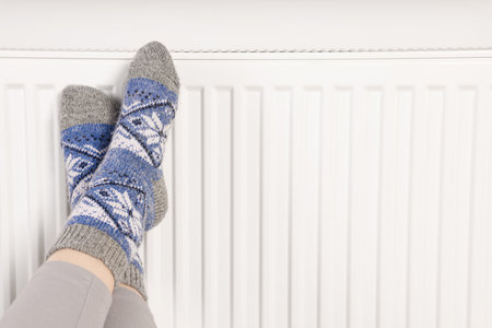 Woman warming feet near heating radiator, closeup. Space for textの写真素材