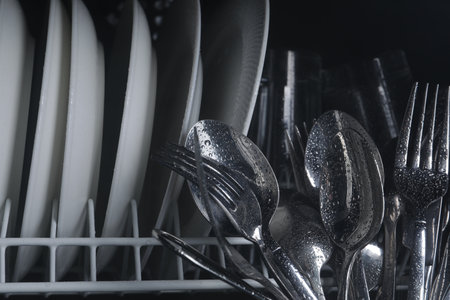 Clean wet plates and cutlery in dishwasher, closeup