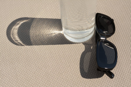 Stylish sunglasses and glass of water on gray surface