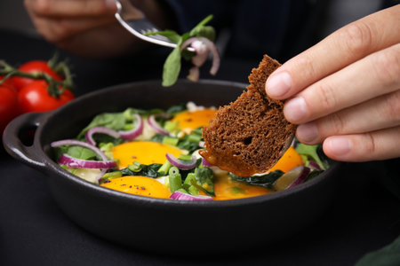 Woman dipping piece of bread into egg yolk, closeup. Eating tasty Shakshukaの写真素材