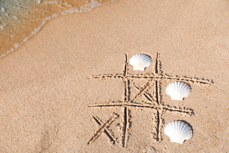 Playing Tic tac toe game with shells on sand near sea, above view. Space for textの写真素材