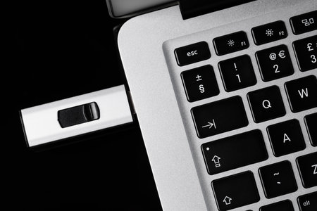 Modern usb flash drive attached to laptop on black table, top view