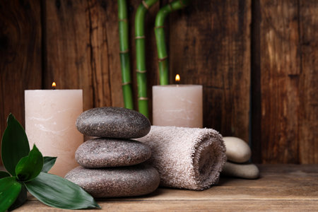 Stacked spa stones, bamboo, candles and towels on wooden table. Space for textの写真素材