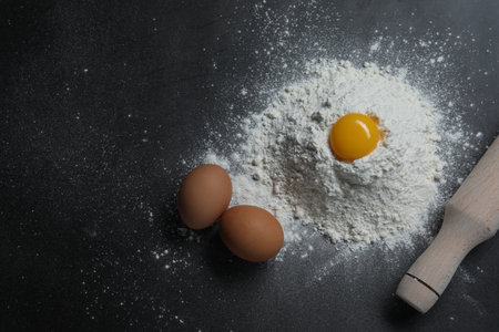 Flour, rolling pin and eggs on black table, flat layの写真素材