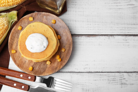 Tasty corn pancakes with sweet kernels and sauce served on white wooden table, flat lay. Space for...