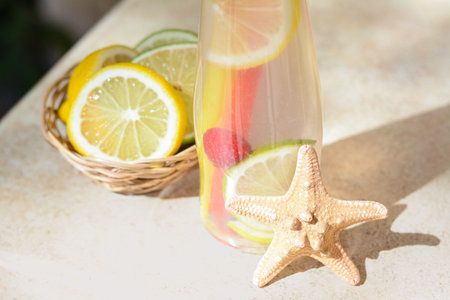 Citrus fruits and refreshing tasty lemonade served in glass bottle on beige table