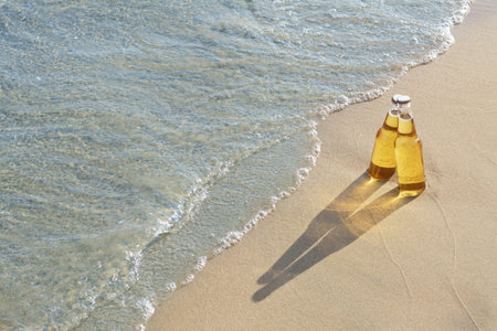 Bottles of cold beer on sandy beach near sea, space for textの写真素材