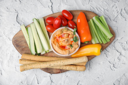 Board with delicious hummus, grissini sticks and fresh vegetables on light gray textured table, top viewの写真素材