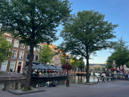 Leiden, Netherlands - August 1, 2022: Beautiful view of city street with outdoor cafe and trees along canalの写真素材