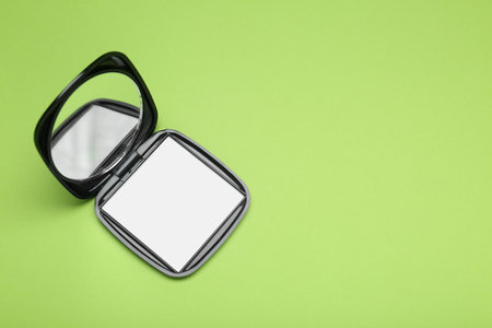 Stylish cosmetic pocket mirror on light green background, top view. Space for text