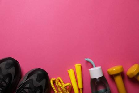 Sneakers, dumbbells and bottle of water on pink background, flat lay with space for text. morning...