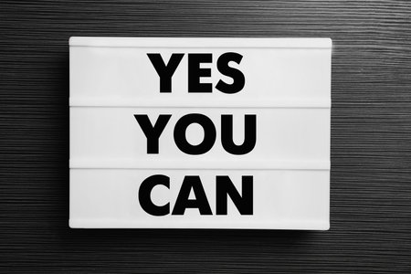 Lightbox with phrase Yes You Can on black wooden table, top view