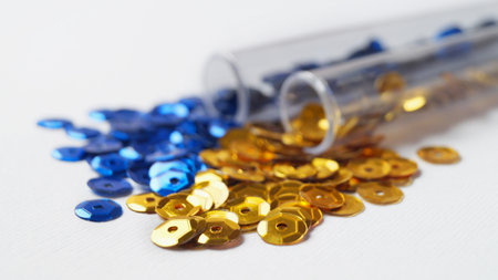Tubes with many blue and golden sequins on white background, closeup