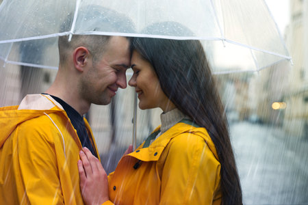 Lovely young couple with umbrella under rain on city street
