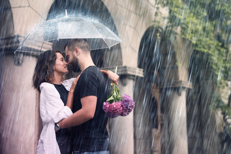 Young couple with umbrella enjoying time together under rain on city streetの写真素材