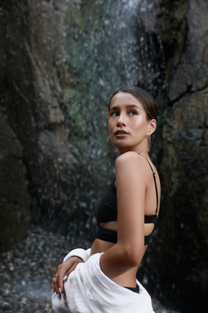 Beautiful young woman in stylish bikini near waterfall outdoors