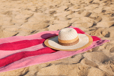 Beach towel and straw hat on sandの写真素材