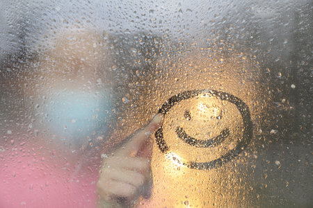 Woman drawing happy face on foggy window at rainy weather, closeupの写真素材