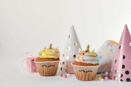 Cute sweet unicorn cupcakes and party hats on white background, space for textの写真素材