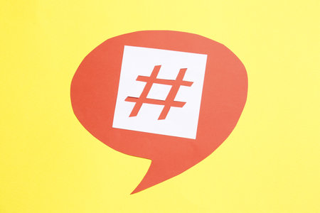 Red paper speech bubble with hashtag symbol on yellow background, top view