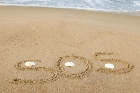 Message SOS drawn on sand near the seaの写真素材