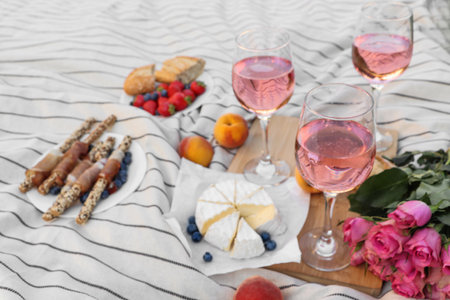 Glasses of delicious rose wine, flowers and food on white picnic blanketの写真素材