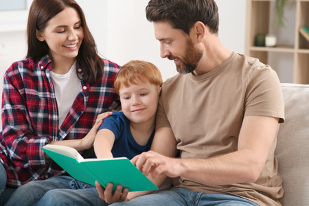Happy parents with their child reading book on couch at homeの写真素材