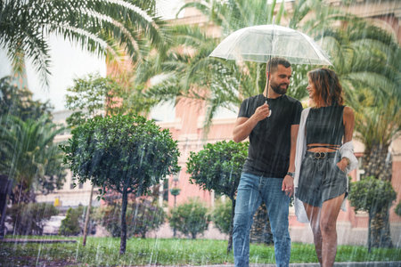 Young couple with umbrella enjoying time together under rain on city streetの写真素材