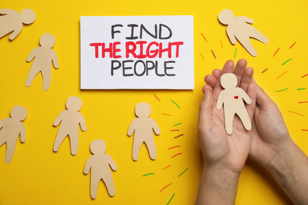 Find the right people. Woman choosing human paper figure with drawn heart among others without it on yellow background, top viewの写真素材