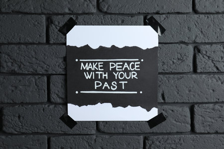 Card with life-affirming phrase Make Peace With Your Past on dark brick wallの写真素材