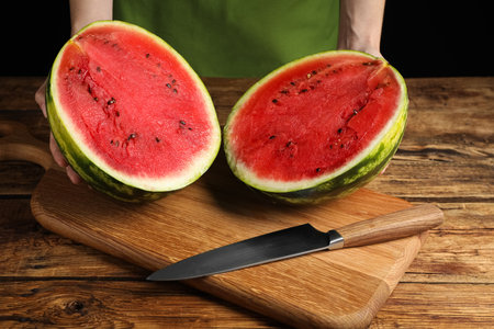 Woman with delicious halved watermelon on wooden table against black background, closeupの写真素材