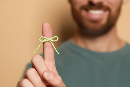 Man showing index finger with tied bow as reminder against beige background, focus on handの写真素材