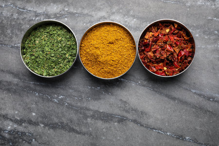 Bowls with dry parsley, turmeric and chili pepper on gray marble table, flat lay. Space for textの写真素材