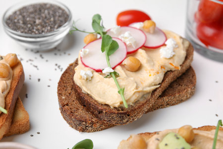 Delicious sandwich with hummus and ingredients on white table