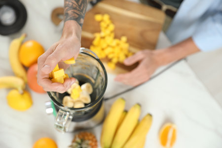 Man adding mango into blender with ingredients for smoothie, top viewの写真素材