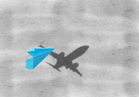 Flying paper plane and shadow of a real airplane on gray backgroundの写真素材